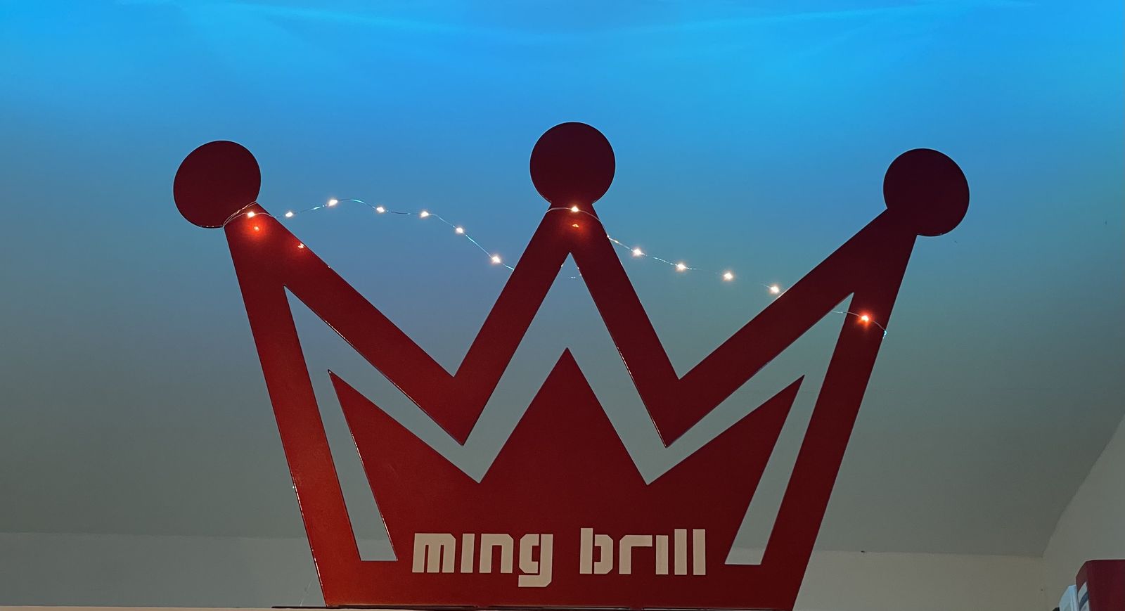 Die rote Ming-Brill-Krone mit Lichterkette vor blau beleuchteter Decke